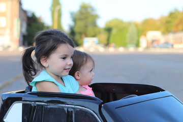 Two amazing girls ride in one big toy car on city street asphalt. Outdoor driving in a summer attraction for children