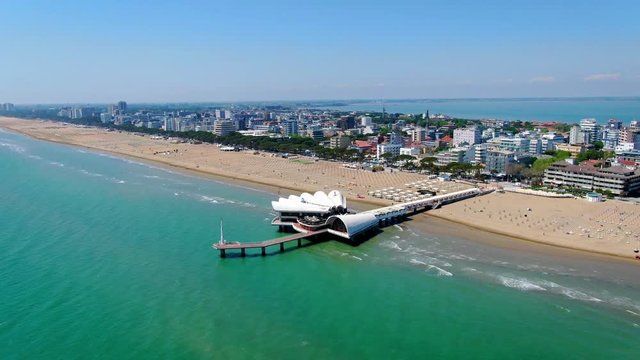 AERIAL: Flying around the beach wooden pier. city of Lignano in the background. Summer vibe. Italy