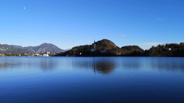 Wide shot lake Bled island Catholic church with waves on water surface, Slovenia