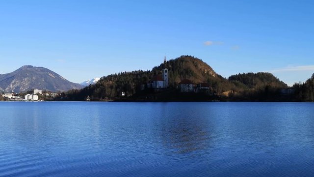 Wide shot lake Bled island Catholic church with waves on water surface, Slovenia