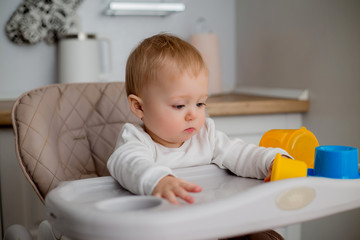 baby is sitting in a high chair, holding an orange. a baby in a high chair drinks water from an orange drinking bowl