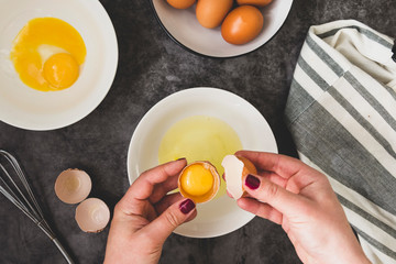 Cooking omlette. Woman's hands cookingomlette, breaking an fresh egg. Dark background. Food flat lay.
