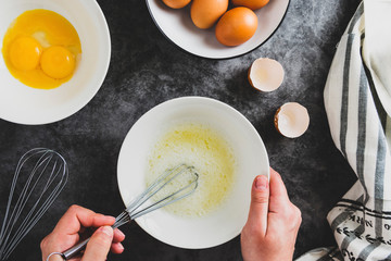 Cooking omlette. Woman's hands cookingomlette, breaking an fresh egg. Dark background. Food flat lay. - obrazy, fototapety, plakaty