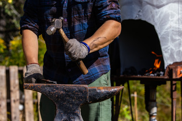 Close up and front midsection view of a blacksmith using traditional hand tools during a metal workshop at a festival celebrating artisans and culture. Selective focus
