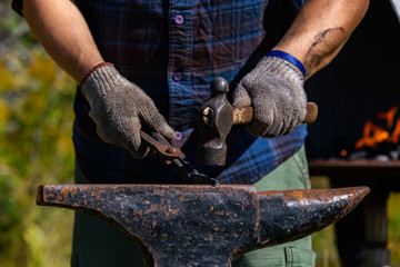 A closeup front midsection view of a masculine blacksmith using a traditional cast iron anvil during a workshop at a festival celebrating artisans. Selective focus shot