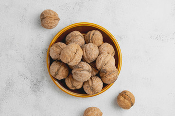 Walnuts in round plate on bright textured surface. Healthy nuts, healthy food.