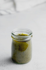 Glass jar with pesto sauce on white textured background table close up. Pasta sauce.