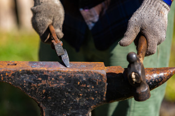 A closeup selective focus view of a metalworker using old fashioned tools during a demonstration at an artisan festival, shaping metal on anvil