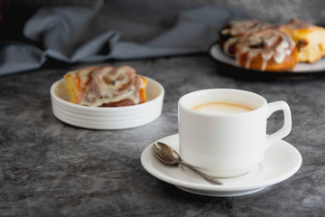 Cup of black coffee and cinnamon roll, cinnabons on background. Dark food photo.