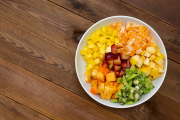Fresh fruits salad - mango, citrus, kiwi fruit, plum and persimmon. Wooden background, flat lay, top view healthy food. Smoothie mix.