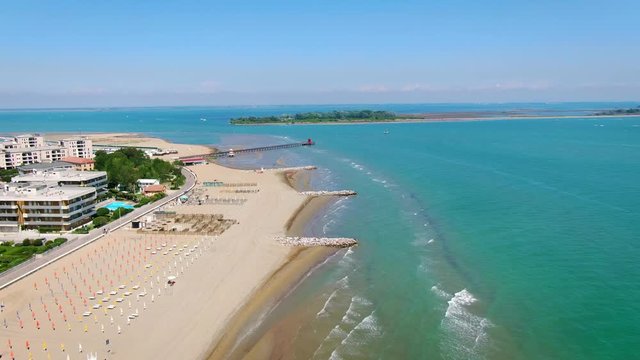 AERIAL: Fly over the beach of Lignano Sabbiadoro, Italy. Red famous lighthouse in the background.