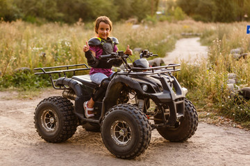 Fototapeta na wymiar Happy little girl playing on road at the day time. He driving on quad bike in the park. Child having fun on the nature. Concept of happiness.