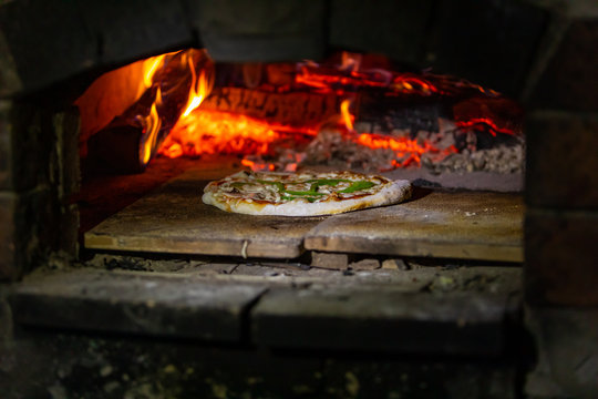 A close up soft focus shot of a traditional wood fired oven, stove cooking fresh handmade pizza at a campsite by night during a multicultural festival