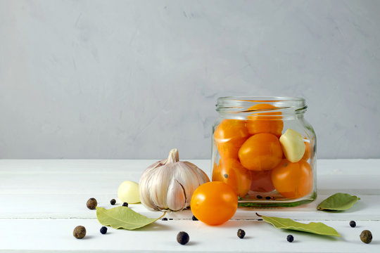pickled yellow cherry tomatoes in a glass jar with spices pepper, garlic on a light background with a place for text. The concept of a healthy diet and a keto diet.