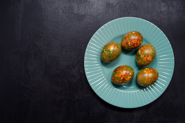 modern trendy marble Easter eggs of original coloring on a blue plate on a black slate background with a place for text.