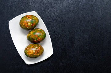 modern trendy marble Easter eggs of original coloring on a white plate on a black slate background closeup with a place for text