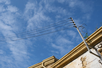 Metal electricity pole and electric wires on top of house roof