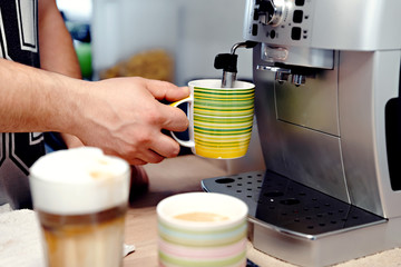home coffee machine pours a mug of coffee,man's hand presses the start button of the coffee machine,hot coffee is poured into a glass,coffee at home