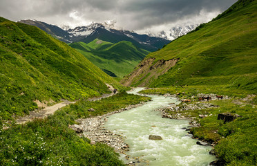 Fototapeta na wymiar Beautiful summer landscape of the Shkhara Glacier valley with Inguri river and snowcapped Caucasus peaks covered in clouds. Upper Svaneti, Georgia.