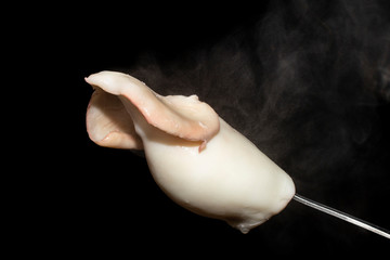 boiled fresh squid on a fork with steam on a black background