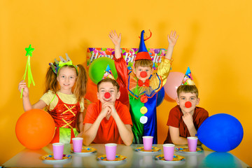 Four children with a clown at the festive table, raise their hands up.