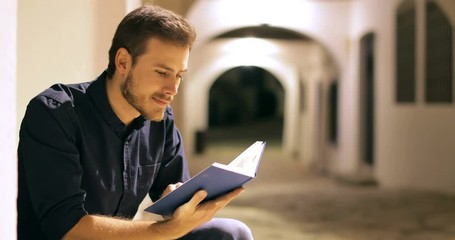 Happy man reading a paper book sitting in the street in the night