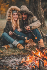 Traveler couple camping and roasting marshmallows over the fire in the forest after a hard day. Concept of trekking, adventure and seasonal vacation.