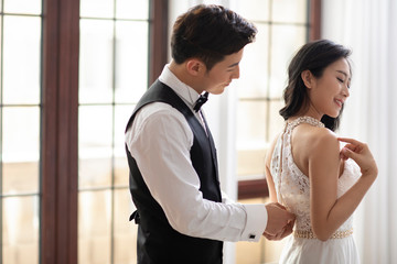Happy young Chinese man zipping up wife's dress at home