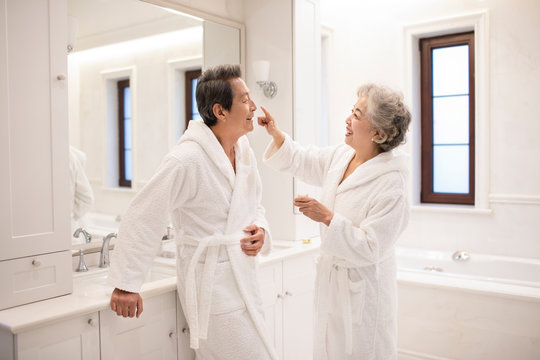 Happy senior Chinese couple applying moisturizer in bathroom
