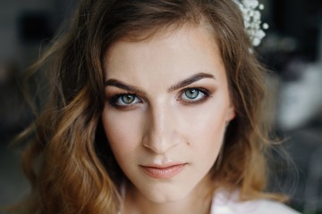 Naklejka premium Close up of attractive woman with beautiful blue eyes and nature make up, curly hairstyle and flower in hair, seriously looking at camera.