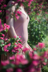  Outdoor photo of pregnant female model in light pink dress standing near blossoming bush.