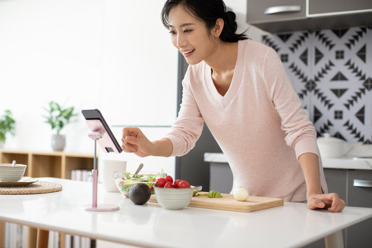 Happy young Chinese woman cooking in kitchen