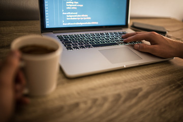 Close-up view of young businessman working on his project while typing programing code on laptop computer in his office room