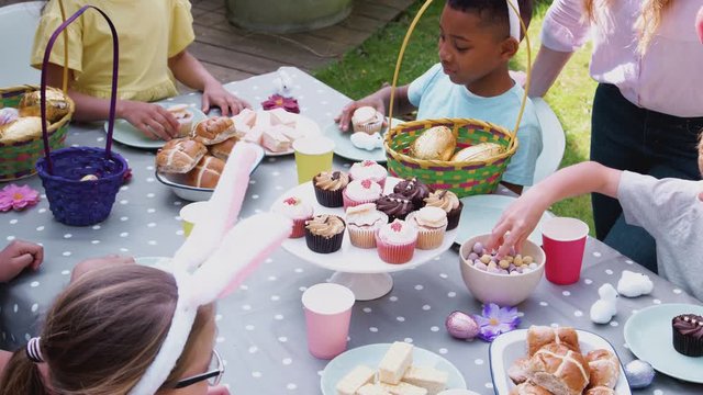 Parents With Children Wearing Bunny Ears Enjoying Outdoor Easter Party In Garden At Home