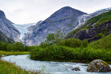 Fototapeta na wymiar Waterfall, river and Briksdalsbreen (Briksdal) glacier. The melting of this glacier forms waterfall and river with clear water. Jostedalsbreenen National Park. Norway.