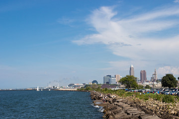 Fototapeta premium Beautiful summer landscape, which depicts the rocky shore of the lake, waves on the water and in the distance are the pain of skyscrapers. View of city of Cleveland,Ohio,USA from the lake Erie