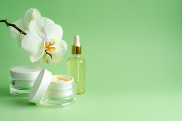 Obraz na płótnie Canvas natural cosmetics anti-aging, anti-wrinkle, for freshness, firmness of the skin. cream, mask, serum, fluid, oil in bottle for face care, with orchids on green background. banner, copy space