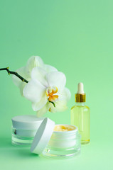 natural anti-aging, for youth cosmetics. cream, mask in jar, serum, fluid, oil in bottle for home, professional face care, with orchids on green background. vertical, pattern, copy space