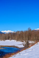 Majestic mountain river in winter over snow mountains and blue sky in Vancouver, Canada.