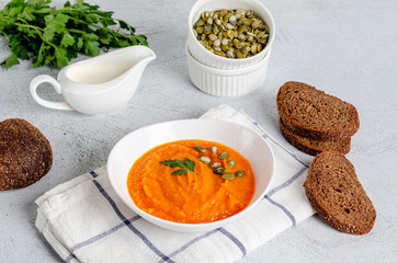Vegetarian autumn cream soup of pumpkins and carrots with seeds and parsley on a gray background.
