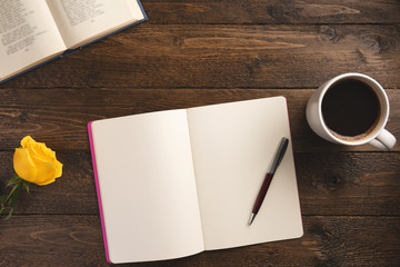 Workplace with open books and cup of coffee. Cup of coffee, flower, notebook, isolated on wooden background. Flat lay, top view, copy space.