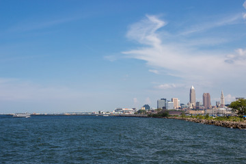 Naklejka premium Beautiful summer landscape, which depicts the rocky shore of the lake, waves on the water and in the distance are the pain of skyscrapers. View of city of Cleveland,Ohio,USA from the lake Erie
