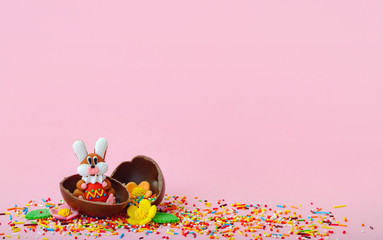 Easter composition. Sweet flowers, sweet bunny and chocolate eggs in foil on pink background with empty place for inspiration.