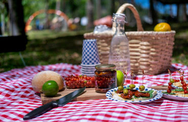 Wicker basket on red checkered tablecloth with fruits and organic food on grass, vegan picnic with healthy food in park outside at summer day