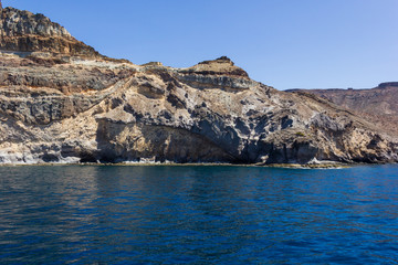 Fototapeta premium Arid rocky landscape by ocean in Gran Canaria, Spain. Canary Islands volcanic coast view from sea. Boat trip, summer vacation concepts