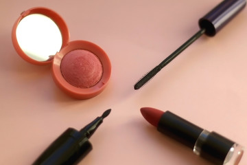 Make-up products on pale pinkbackground: pink blush, mascara, eyeliner and lipstick. Selective focus.