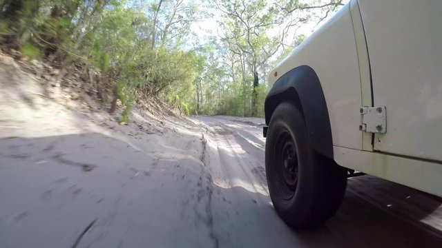 Stunning stabilized action low angle footage of an old four-wheel drive off-road vehicle driving through a forest on an inland sand track on Fraser Island off the coast of Queensland, Australia