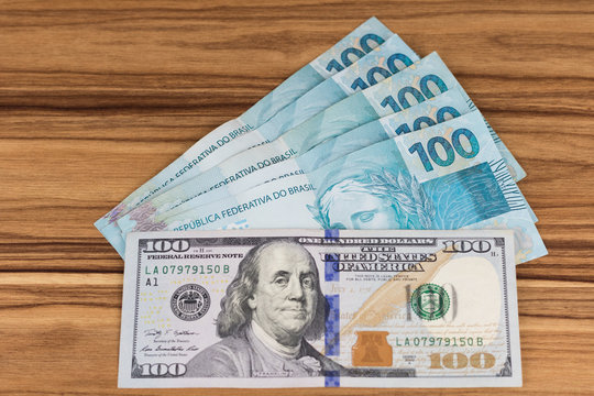 One hundred US dollar bills and one hundred Brazilian reais banknotes, business finance shopping concept.