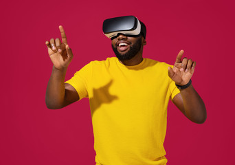 Naklejka premium Smiling man interacting with invisible screen while having virtual reality experience on red background