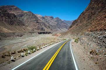 Highway road in the Andes mountains along canyon river. Empty road in arid climate as desert with rocky terrain. Curved road with yellow dividing line  through mountains in Mendoza province, Argentina